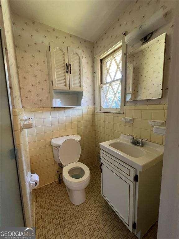 bathroom featuring tile patterned floors, vanity, toilet, and tile walls