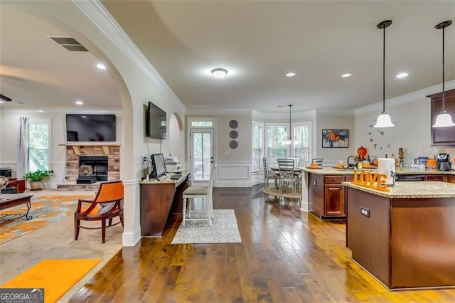 kitchen with decorative light fixtures, light stone counters, ornamental molding, and a fireplace