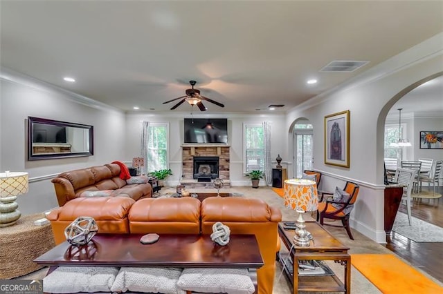 living room featuring hardwood / wood-style flooring, ceiling fan, a stone fireplace, and crown molding