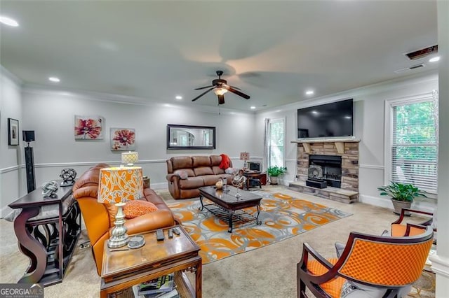 carpeted living room featuring a stone fireplace, ceiling fan, plenty of natural light, and ornamental molding