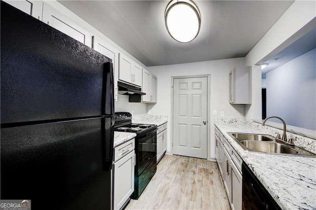 kitchen featuring light stone countertops, light wood-type flooring, sink, black appliances, and white cabinets