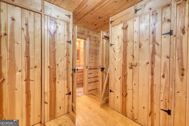 hallway featuring wood walls, wooden ceiling, and light hardwood / wood-style flooring