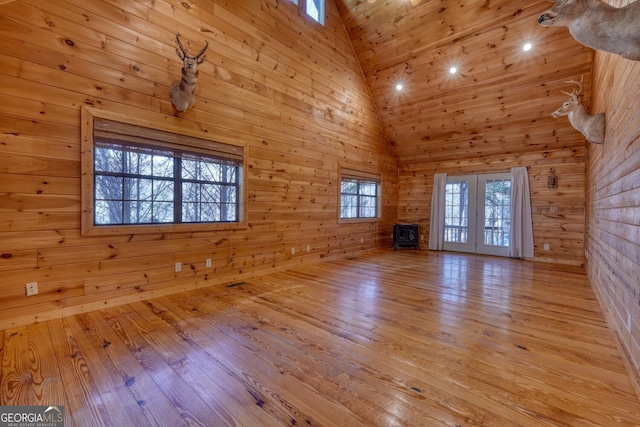 unfurnished living room with french doors, light wood-type flooring, high vaulted ceiling, wooden ceiling, and wood walls