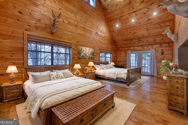 bedroom with wooden walls, light wood-type flooring, high vaulted ceiling, and wooden ceiling