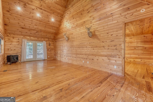 unfurnished living room with a wood stove, high vaulted ceiling, french doors, and wood walls