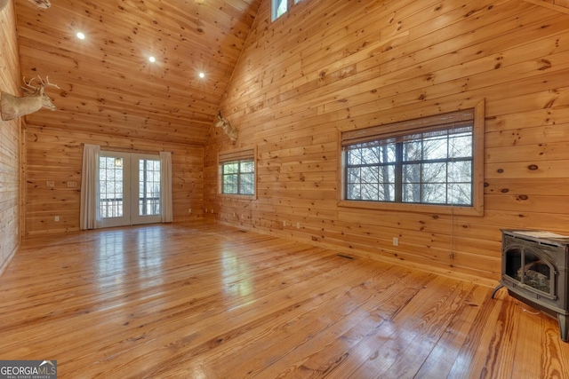 unfurnished living room with wood walls, a wood stove, high vaulted ceiling, french doors, and light wood-type flooring