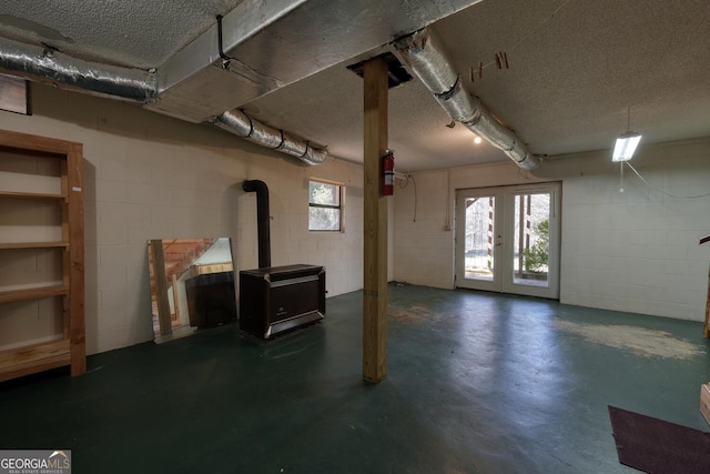 basement with french doors, a textured ceiling, and a wood stove