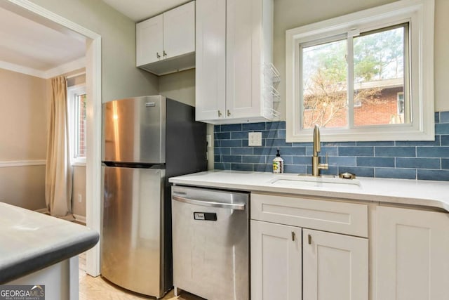 kitchen with decorative backsplash, light stone counters, stainless steel appliances, sink, and white cabinetry