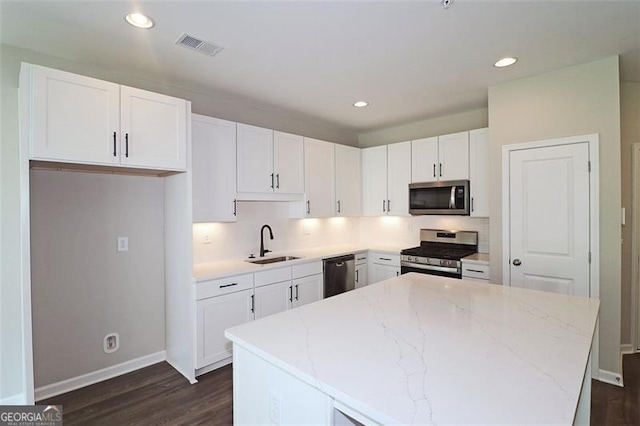 kitchen with light stone countertops, stainless steel appliances, sink, white cabinets, and a center island