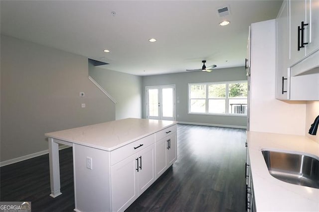 kitchen featuring a kitchen island, light stone countertops, white cabinetry, and sink