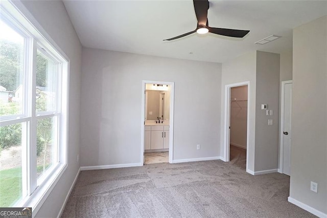 unfurnished bedroom with light carpet, a walk in closet, ceiling fan, connected bathroom, and a closet