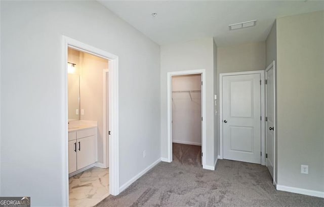 unfurnished bedroom with ensuite bathroom, a spacious closet, a closet, and light colored carpet