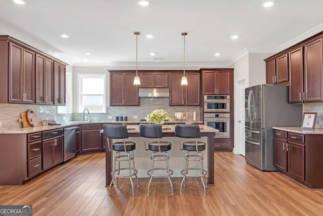 kitchen featuring stainless steel appliances, crown molding, decorative light fixtures, a center island, and a breakfast bar area