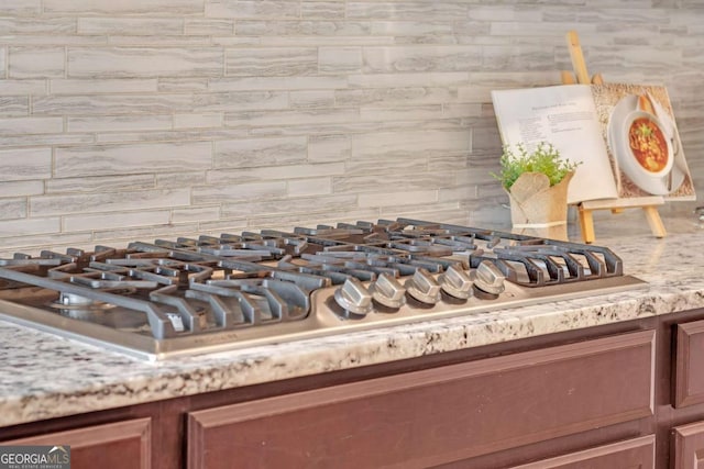 interior details with stainless steel gas stovetop, light stone counters, and backsplash