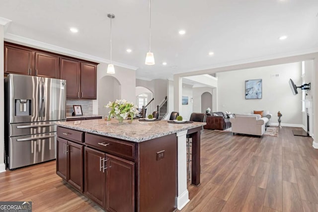 kitchen featuring a center island, stainless steel refrigerator with ice dispenser, ornamental molding, decorative light fixtures, and light stone counters