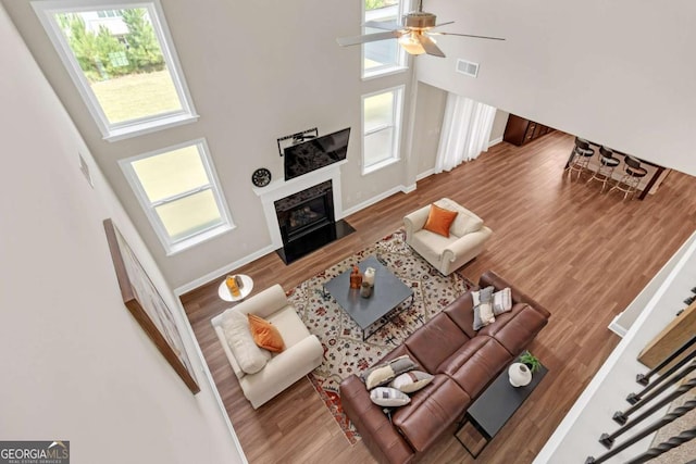 living room with ceiling fan, wood-type flooring, and a high ceiling