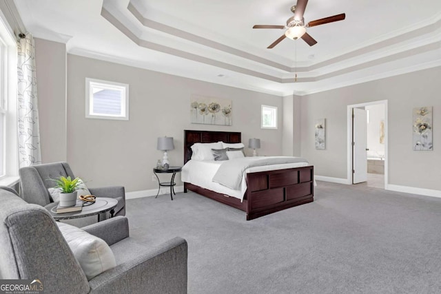 carpeted bedroom with a raised ceiling, connected bathroom, ceiling fan, and ornamental molding