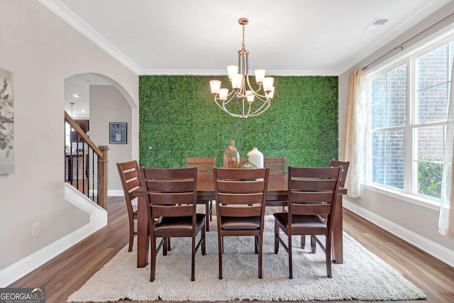 dining area featuring a healthy amount of sunlight, hardwood / wood-style flooring, ornamental molding, and an inviting chandelier