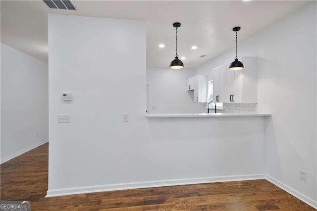 kitchen with white cabinets, kitchen peninsula, tasteful backsplash, and dark wood-type flooring