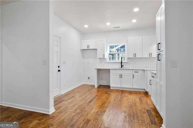 kitchen with sink, light wood-type flooring, white cabinetry, and backsplash