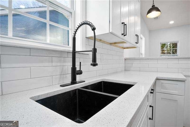 kitchen featuring white cabinets, light stone countertops, sink, and hanging light fixtures