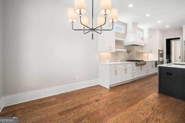 kitchen featuring sink, hanging light fixtures, custom range hood, white cabinets, and backsplash