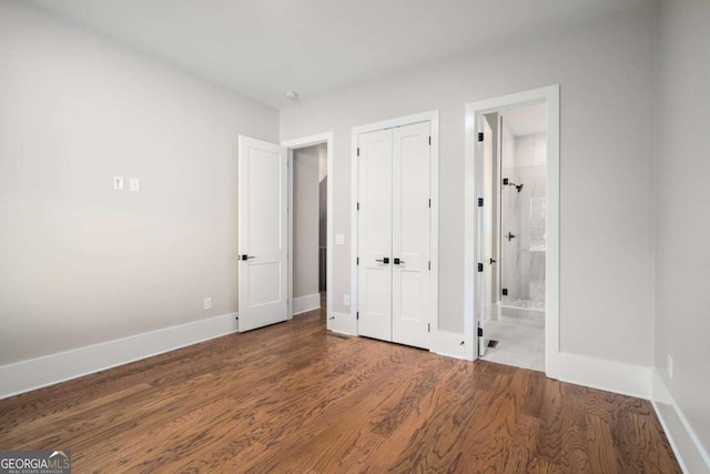 unfurnished bedroom featuring ensuite bathroom, dark hardwood / wood-style floors, and a closet