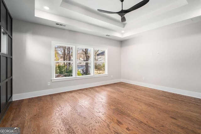 spare room with a raised ceiling, hardwood / wood-style floors, and ceiling fan