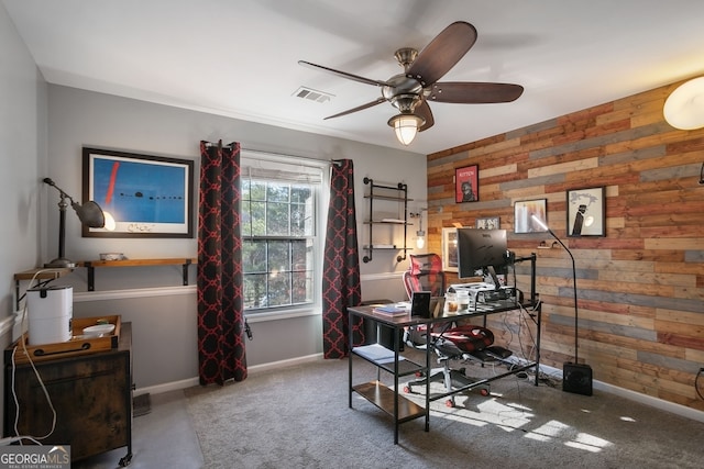 carpeted office featuring wooden walls and ceiling fan