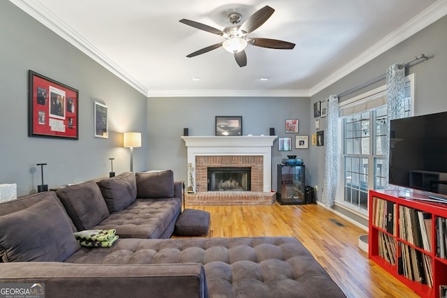 living room with hardwood / wood-style flooring, ceiling fan, ornamental molding, and a brick fireplace