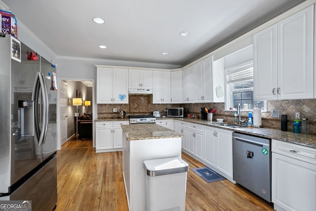 kitchen with light stone countertops, appliances with stainless steel finishes, sink, a center island, and white cabinetry