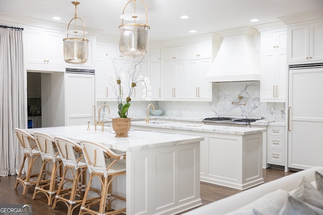 kitchen featuring premium range hood, white cabinetry, paneled refrigerator, and a center island with sink