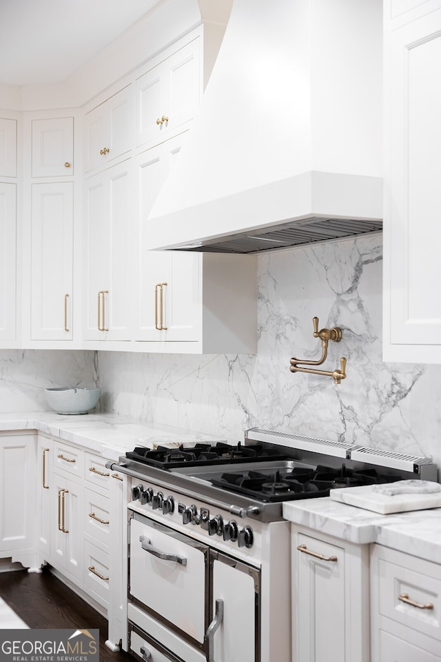 kitchen featuring premium range hood, gas stove, white cabinetry, tasteful backsplash, and light stone countertops