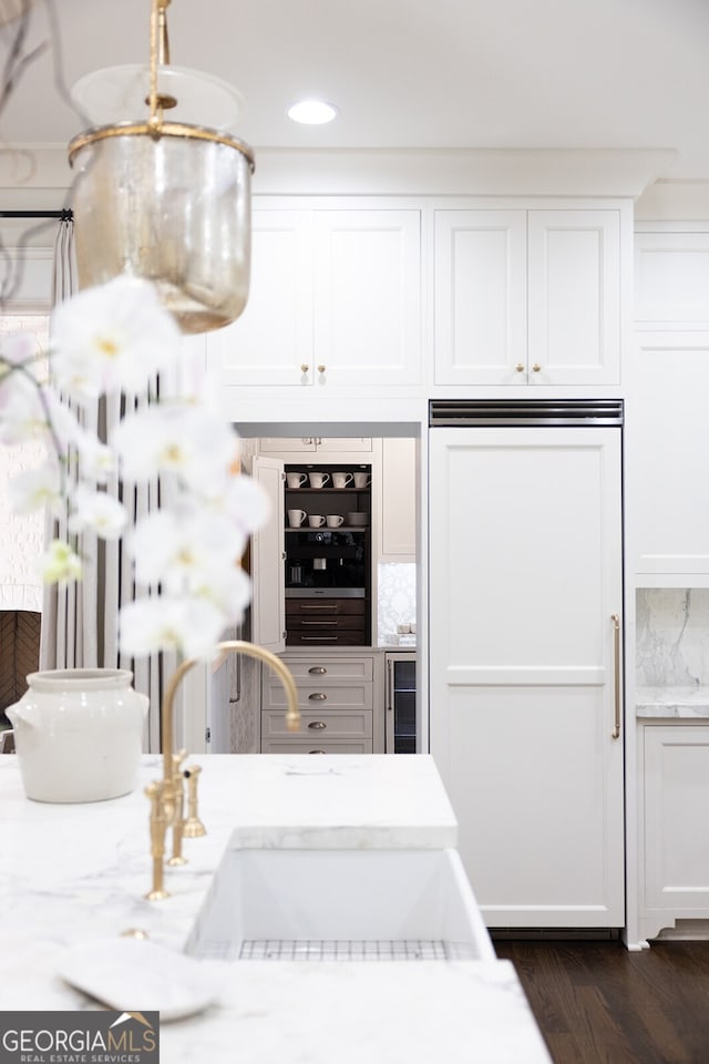 kitchen featuring sink, paneled built in refrigerator, light stone counters, wine cooler, and white cabinets