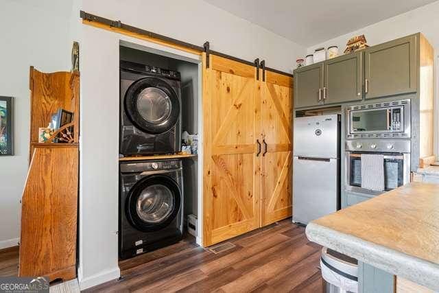 laundry room with stacked washer and dryer, dark hardwood / wood-style flooring, and a barn door