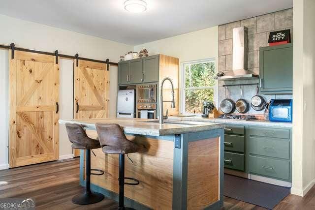 kitchen featuring a kitchen breakfast bar, green cabinets, sink, a barn door, and wall chimney range hood