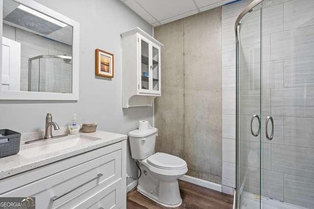 bathroom featuring a shower with door, a paneled ceiling, hardwood / wood-style floors, toilet, and vanity