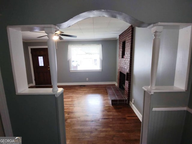 unfurnished living room featuring a brick fireplace, ornamental molding, dark hardwood / wood-style floors, and ceiling fan