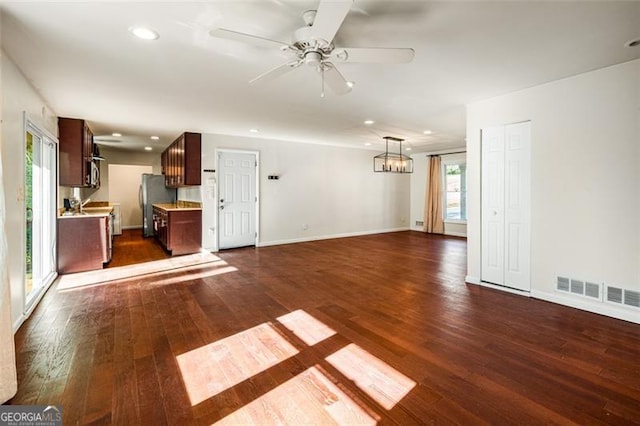 unfurnished living room featuring ceiling fan with notable chandelier and dark hardwood / wood-style floors