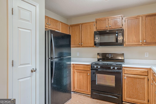 kitchen with light hardwood / wood-style floors, a textured ceiling, and black appliances