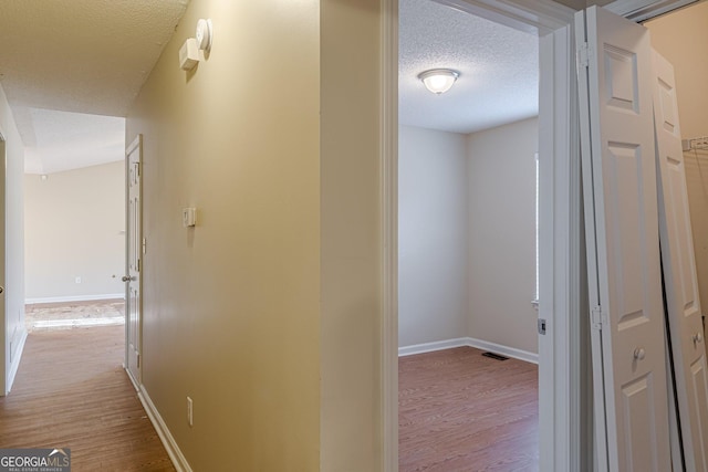 hallway with a textured ceiling and light hardwood / wood-style floors