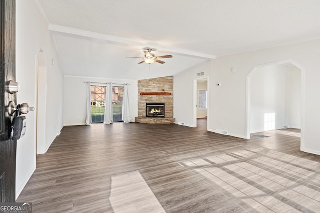 unfurnished living room featuring ceiling fan, a stone fireplace, lofted ceiling with beams, and wood-type flooring