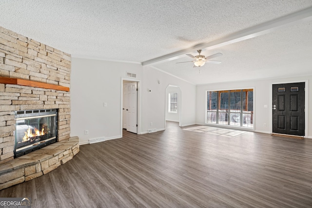 unfurnished living room featuring a textured ceiling, ceiling fan, a stone fireplace, and dark wood-type flooring