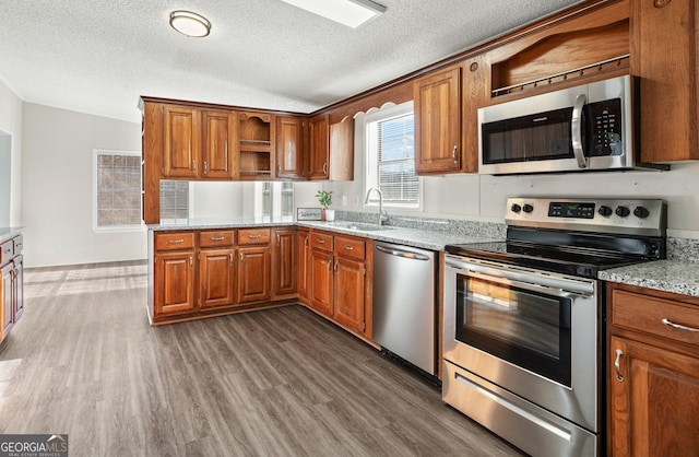 kitchen with stainless steel appliances, sink, a textured ceiling, light stone countertops, and dark wood-type flooring