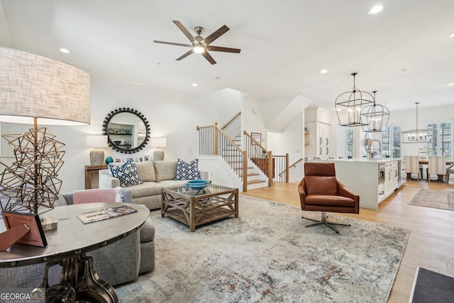 living room with ceiling fan with notable chandelier, sink, crown molding, and light hardwood / wood-style flooring