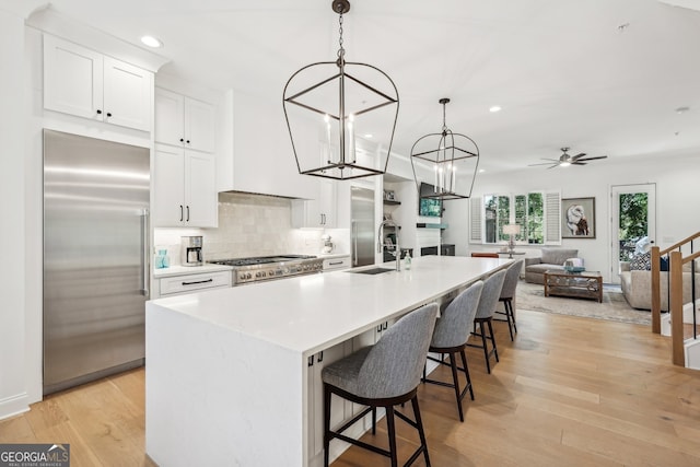 kitchen with white cabinets, ceiling fan, stainless steel built in fridge, and a kitchen island with sink