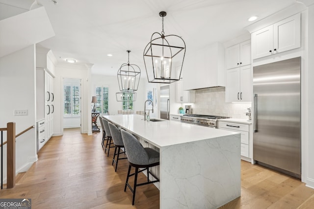 kitchen featuring a kitchen island with sink, sink, pendant lighting, high quality appliances, and white cabinetry