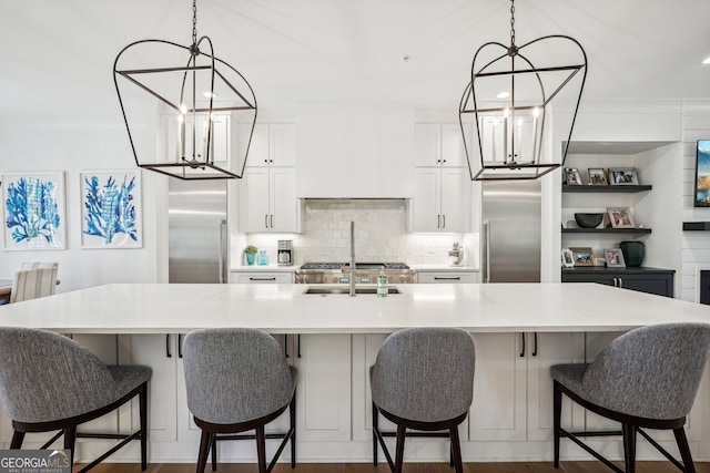 kitchen with white cabinetry, a large island with sink, stainless steel fridge, and hanging light fixtures