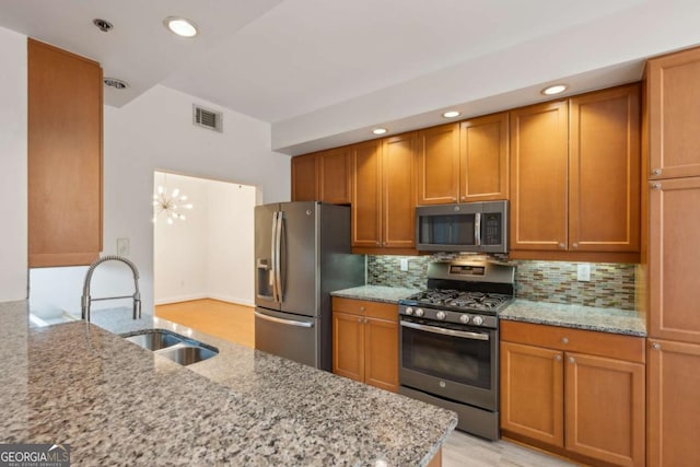 kitchen with backsplash, an inviting chandelier, sink, light stone countertops, and appliances with stainless steel finishes