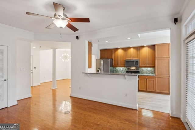 kitchen featuring backsplash, ceiling fan with notable chandelier, ornamental molding, kitchen peninsula, and stainless steel appliances